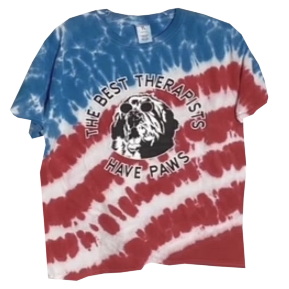 Red, white, and blue tie-dye T-shirt with the text "The Best Therapists Have Paws" surrounding a graphic of a dog wearing sunglasses.