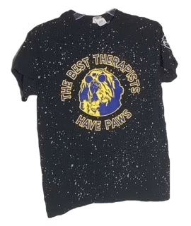 Black T-shirt featuring a splattered paint design with a graphic of a golden dog in a blue circle and the text "THE BEST THERAPISTS HAVE PAWS" in yellow.