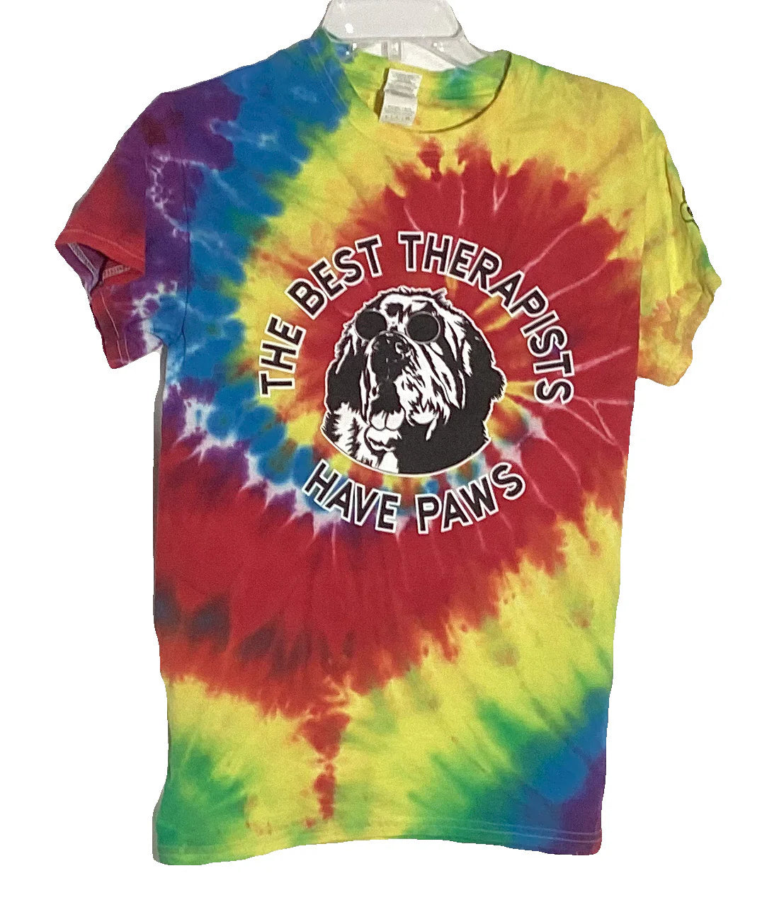 Colorful tie-dye t-shirt featuring the text "The Best Therapists Have Paws" encircling a graphic of a dog's face, displayed on a hanger.