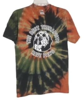 A tie-dye T-shirt featuring "The Best Therapists Have Paws" text and a paw print graphic in shades of green and orange.
