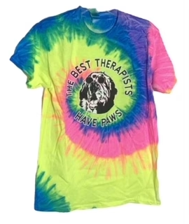 Alt text: "Colorful tie-dye t-shirt featuring a 'The Best Therapists Have Paws' slogan with a paw print and dog silhouette, displayed on a white background."