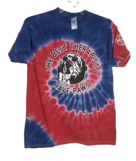 Blue and red tie-dye T-shirt featuring a graphic of a dog with the phrase "The Best Therapists Have Paws" in white text, displayed on a circular black background.